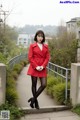 A woman in a red coat is standing on a sidewalk.