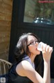 A woman wearing glasses drinking from a water bottle.