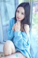 A woman in a blue sweater sitting on a window sill.