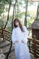 A woman in a white robe standing on a wooden bridge.