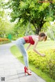 A woman in a red top and jeans bending over in a park.