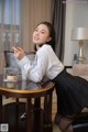 A woman in a white shirt and black skirt sitting at a table.