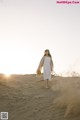 A woman in a white dress standing in the sand.