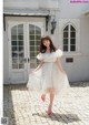 A woman in a white dress and pink shoes standing in front of a building.