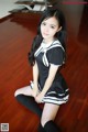 A woman in a black and white dress sitting on a wooden floor.