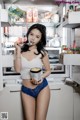 A woman standing in front of an open refrigerator holding a cup of ice cream.