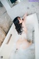 A naked woman laying in a bathtub filled with foam.