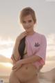 A woman in a pink shirt is posing on the beach.