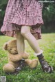 A little girl in a red and white checkered dress holding a teddy bear.