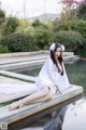 A woman in a white dress sitting on a dock by a pool.