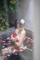 A woman sitting in a bathtub with rose petals on the floor.